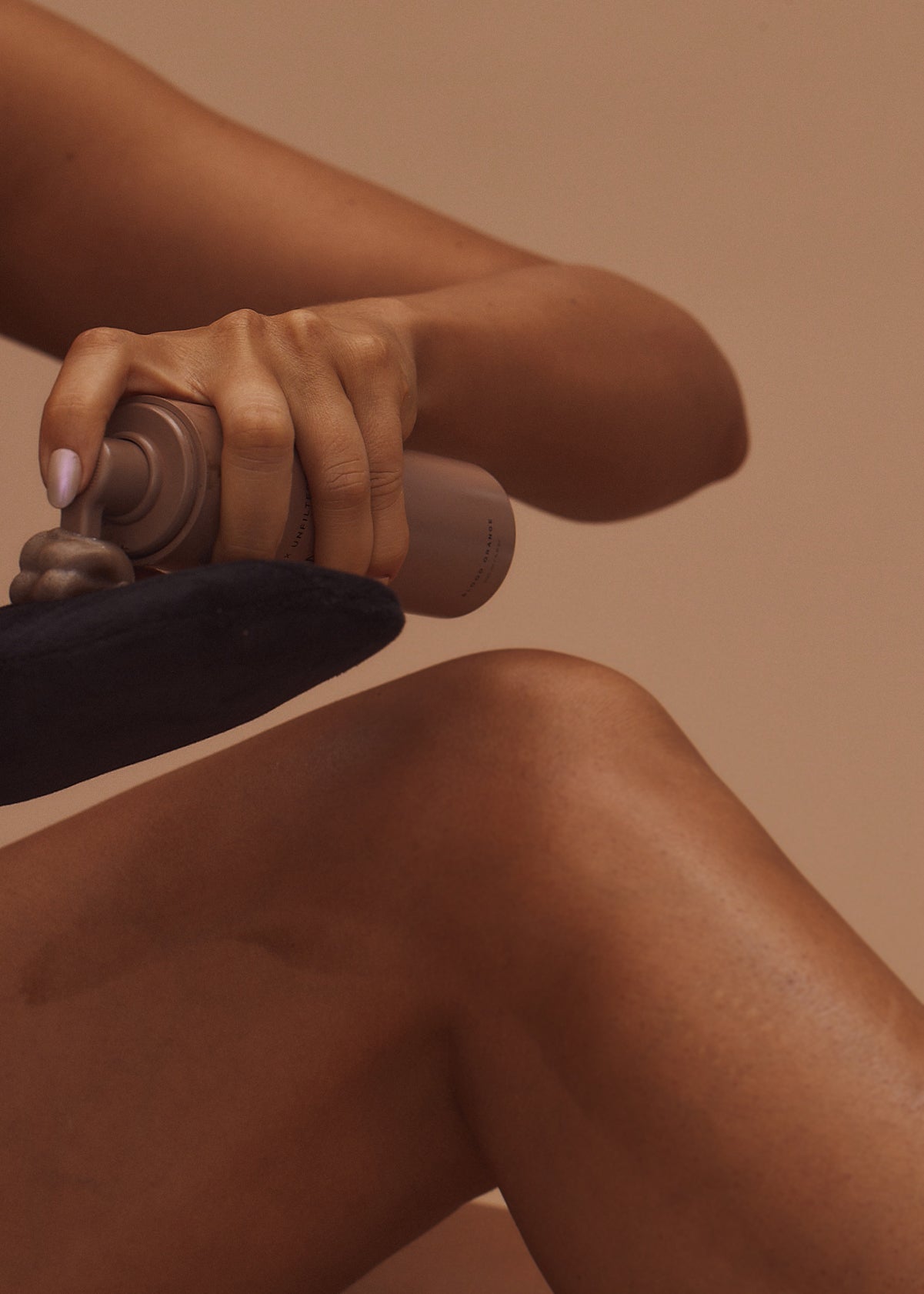 Hand dispensing self-tanning mousse from a bottle onto an applicator mitt above a tanned knee.