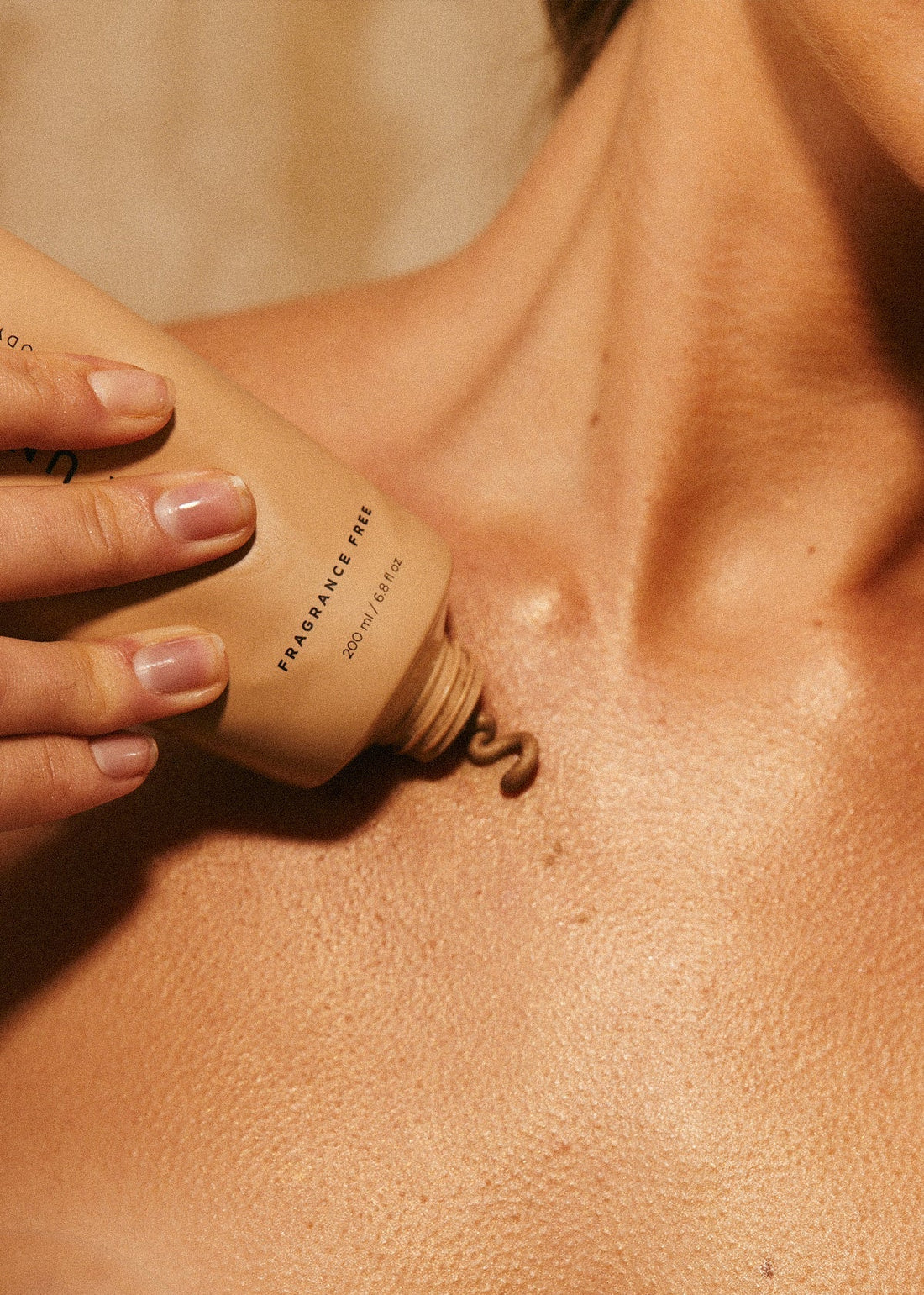 Hand applying beige lotion from a tube labeled FRAGRANCE FREE 200 ml / 6.8 fl oz onto chest