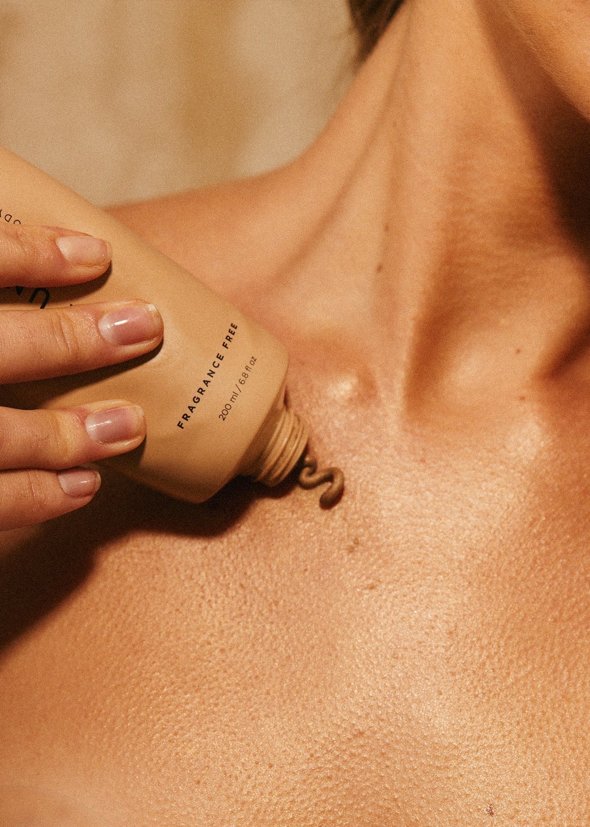 Hand applying beige lotion from a tube labeled FRAGRANCE FREE 200 ml / 6.8 fl oz onto chest