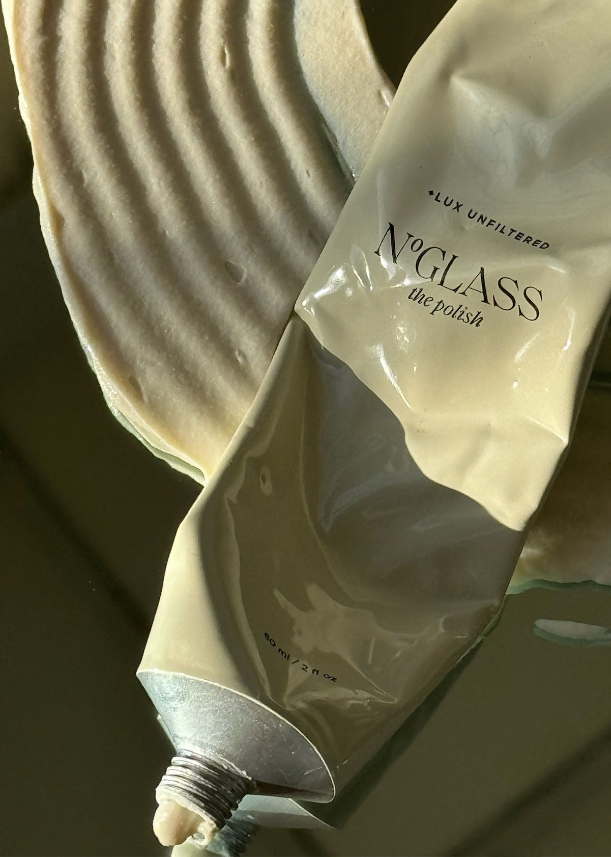 Squeezed beige tube on mirror labeled NOGLASS the polish, LUX UNFILTERED, 60 ml / 2 fl oz