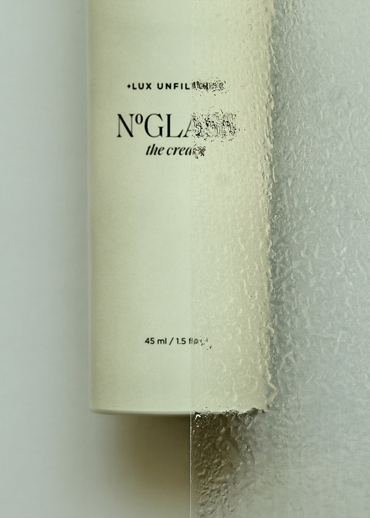 Skincare bottle labeled LUX UNFIL, NºGLA, the cream, 45 ml / 1.5 fl oz seen through textured glass