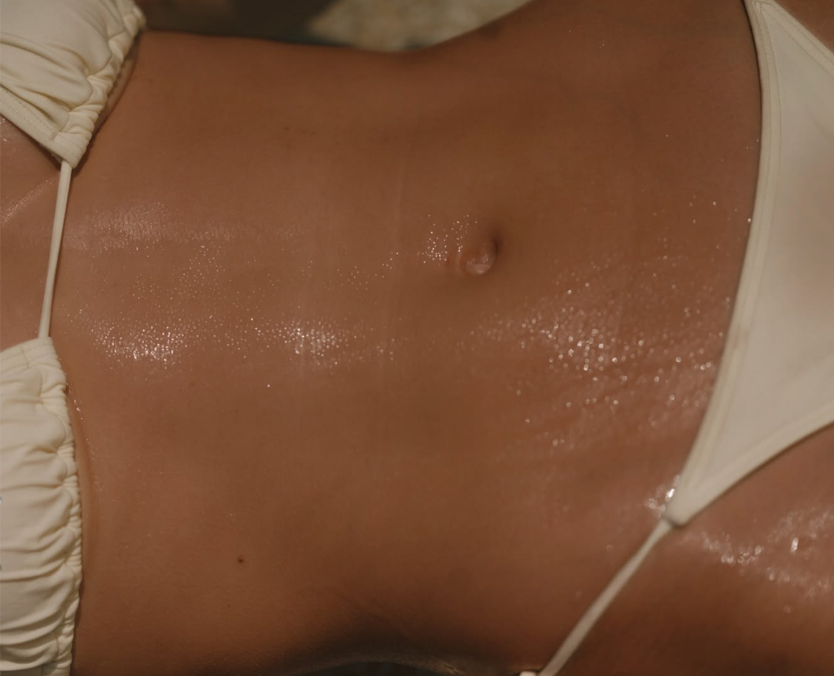 Close-up of a person in a white bikini with glistening, bronzed skin