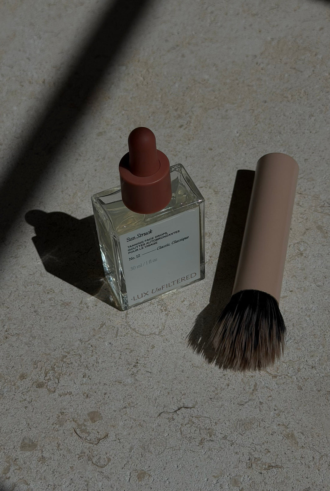 Close-up of Sun Struck tanning face drops bottle with a makeup brush on a stone surface