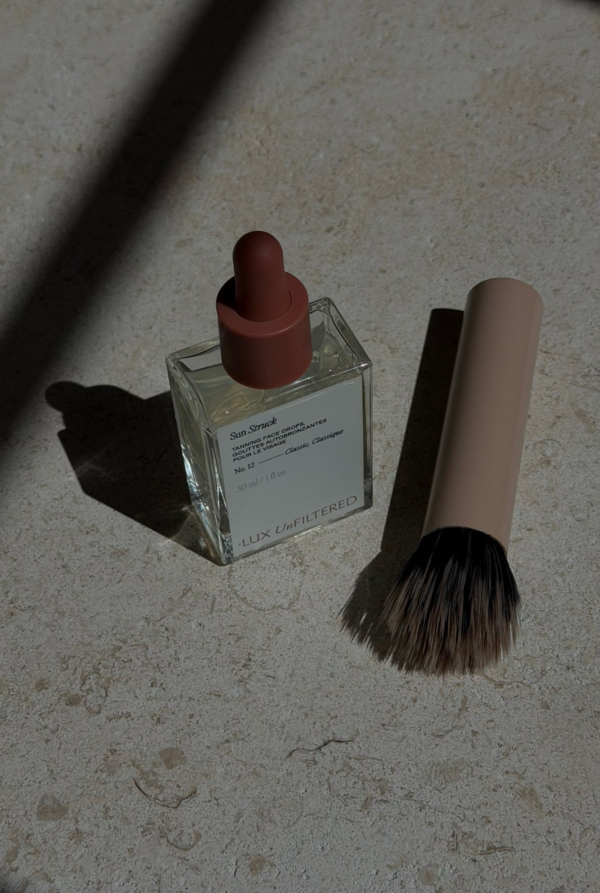 Close-up of Sun Struck tanning face drops bottle with a makeup brush on a stone surface