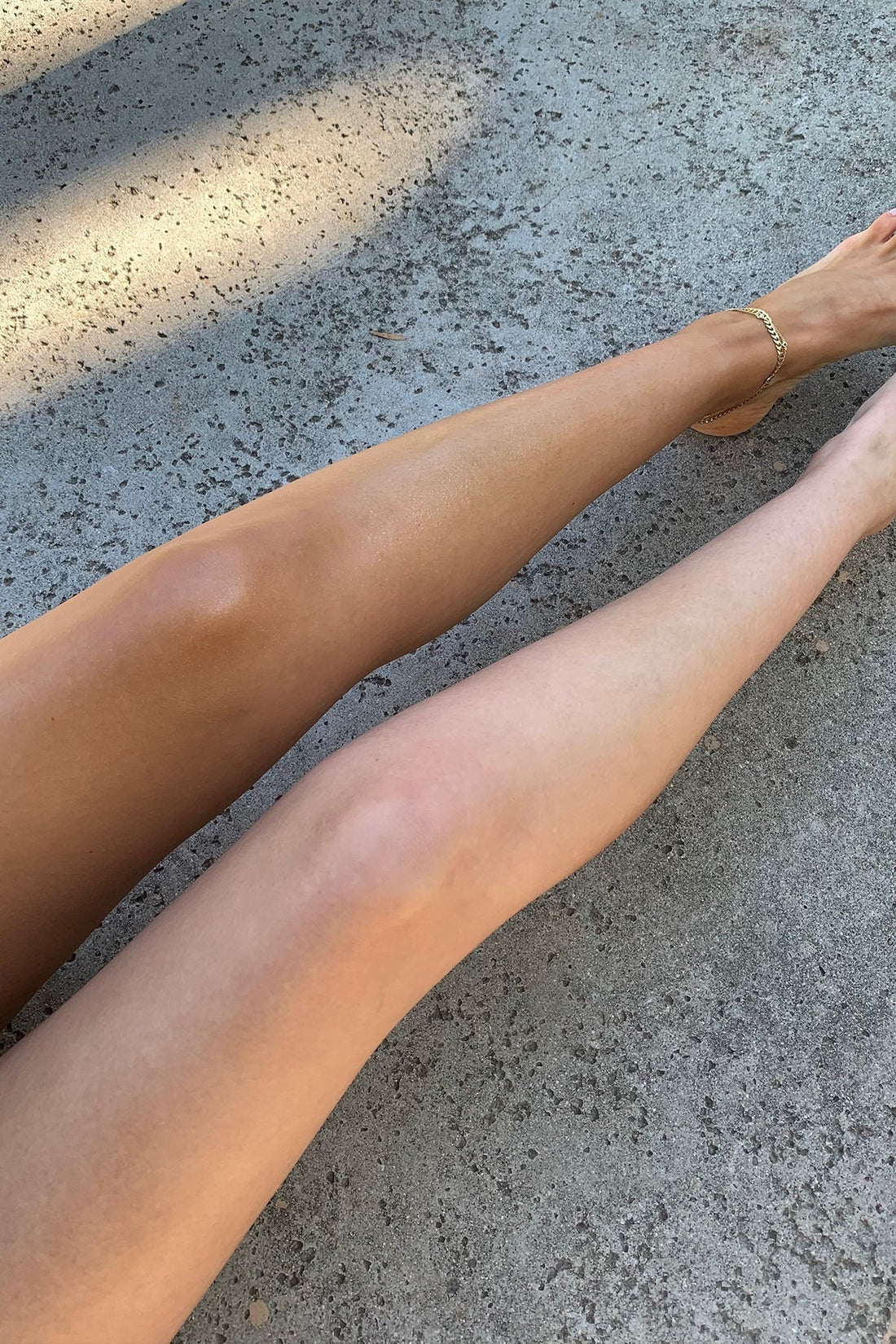 Two legs side-by-side showing one deep self-tan and one untanned leg resting on a concrete surface