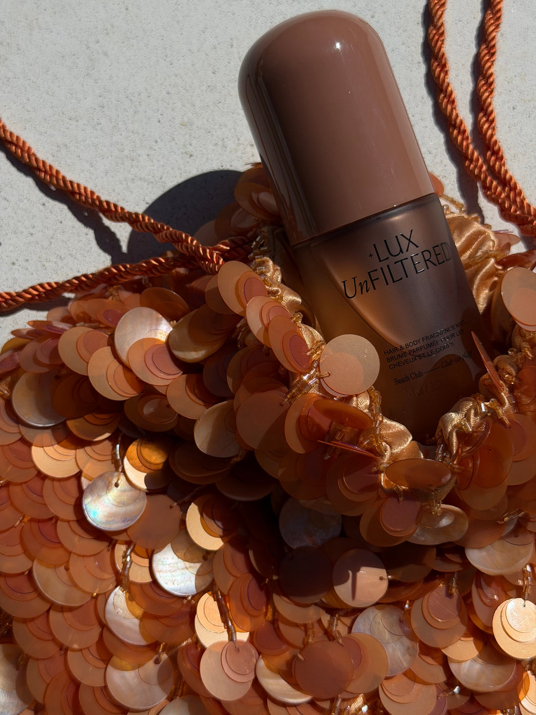 Close-up of Beach Club hair and body fragrance mist bottle with brown packaging on a sequined background