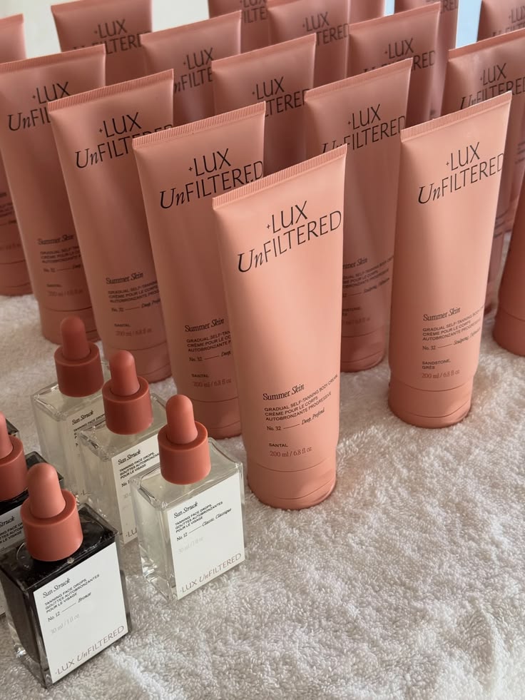 Close-up of LUX Unfiltered Summer Skin self-tanning cream tubes and Skin Stuck dropper bottles on a white towel