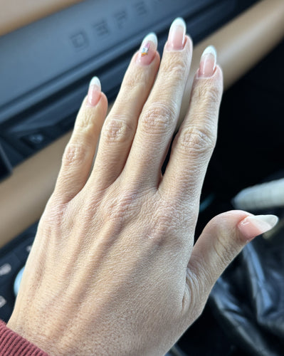 Left hand showing long clear-tipped French manicure with tiny flower nail decal on ring finger.
