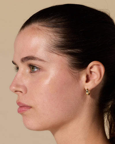 Left-profile close-up of a young woman with pulled-back dark hair, clear skin, and a small gold hoop earring.