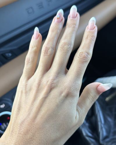 Left hand with long French-tip acrylic nails; ring finger shows small Daisy Duck sticker, photographed inside a car.