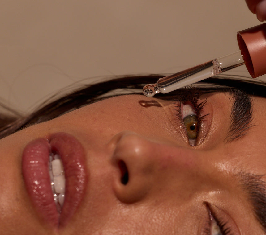 Person uses a dropper to apply skincare product near the eye in a close-up beauty scene