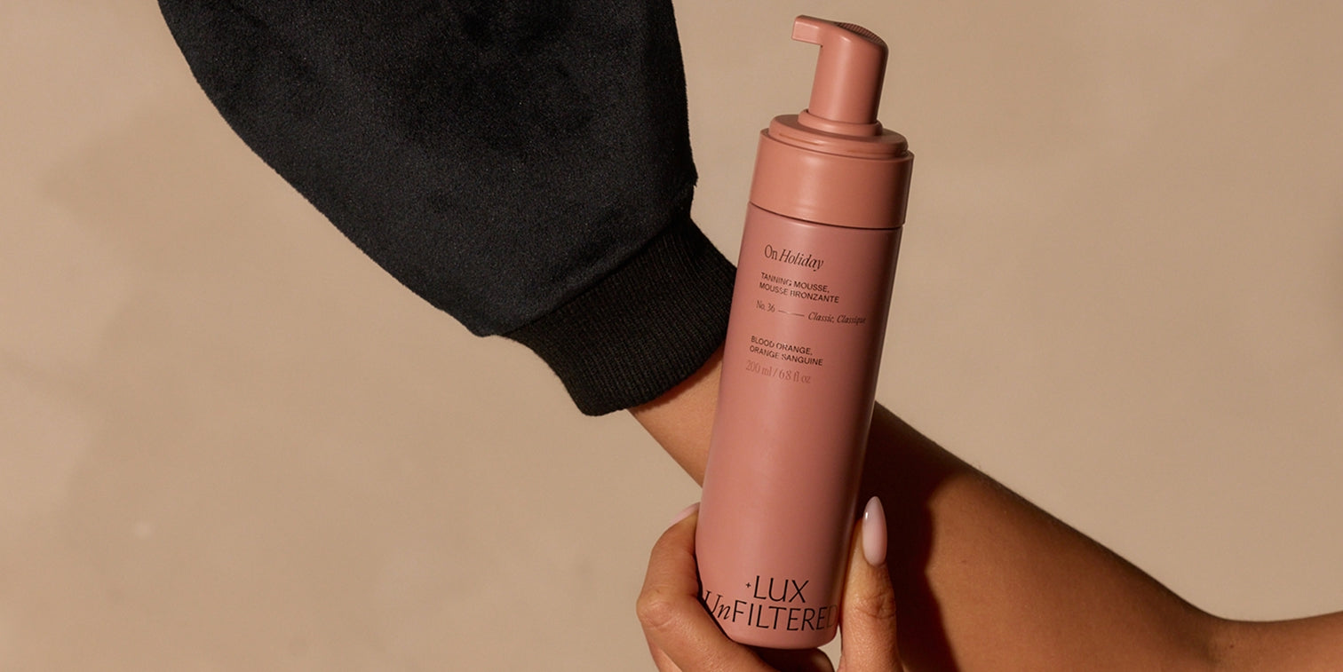 Hand holding dusty-rose pump bottle labeled 'On Holiday; BLOOD ORANGE; LUX UnFILTERED; 200 ml / 6.8 fl oz'