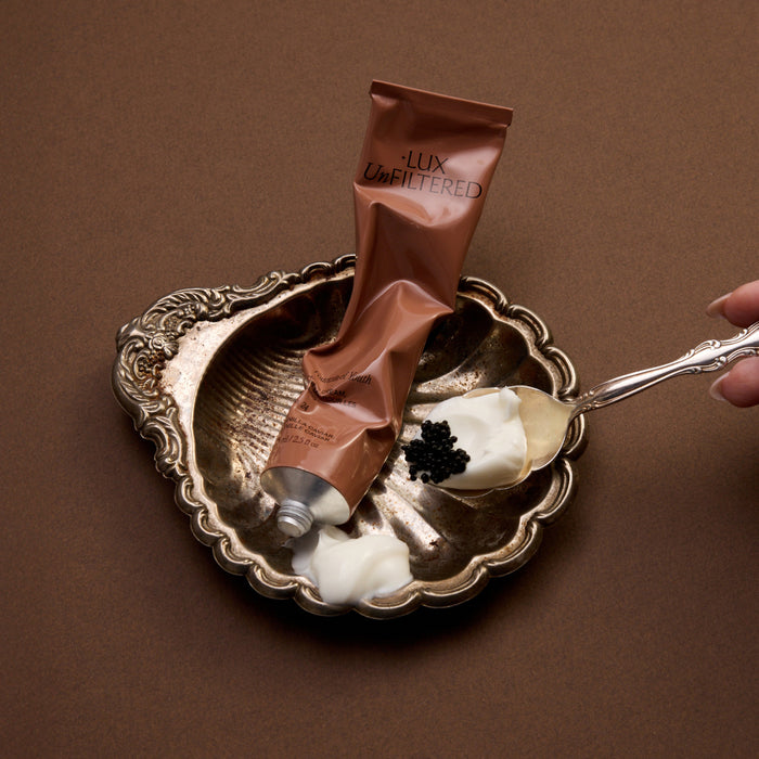 Crushed tube labeled '+LUX UnFILTERED' in an ornate silver dish with cream and a spoon topped with black caviar.