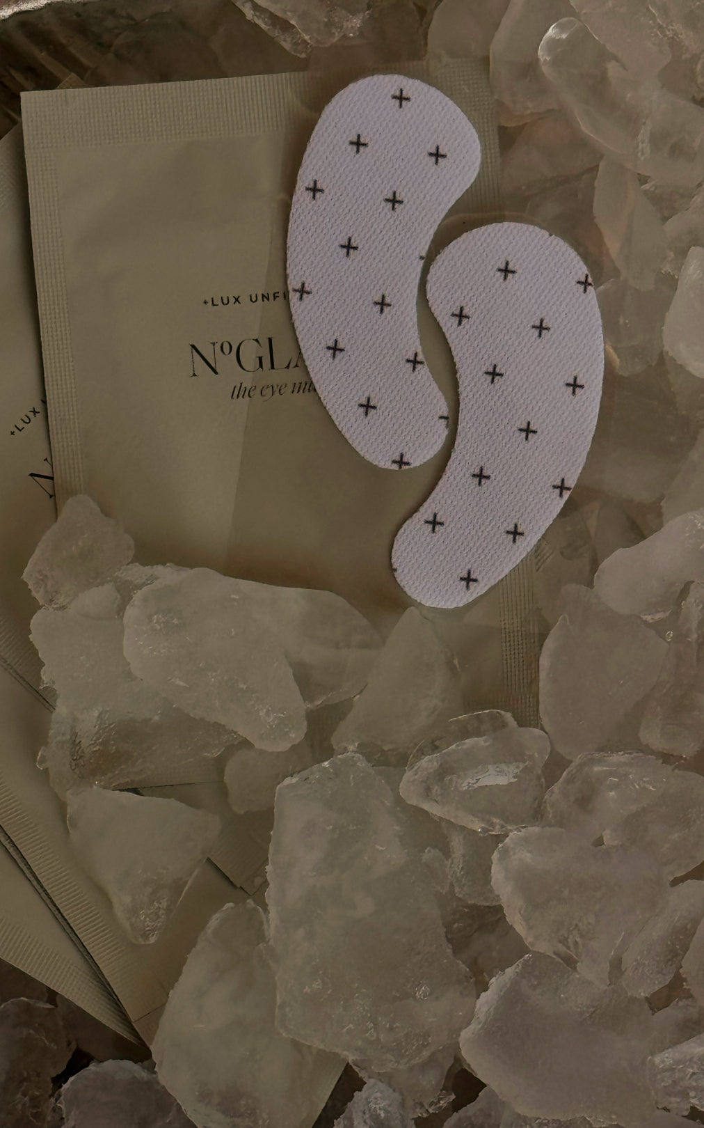 Two crescent eye patches with black plus pattern on a packet labeled + LUX UNFILTERED NO GLAM the eye mask