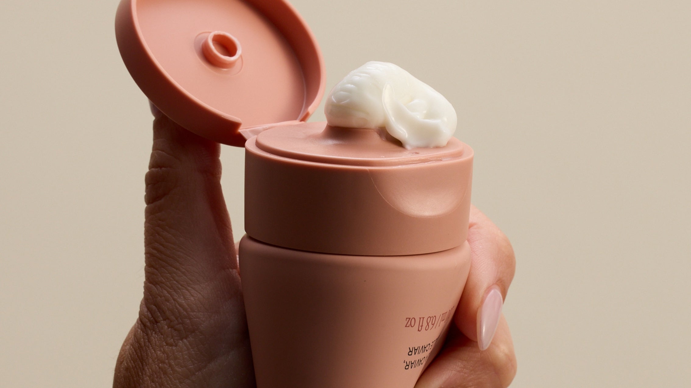 Hand holding a peach-colored flip-top squeeze tube with a dollop of white cream on the cap
