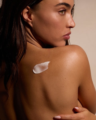 Female's bare upper back and shoulder with a dollop of cream; she looks over her shoulder.