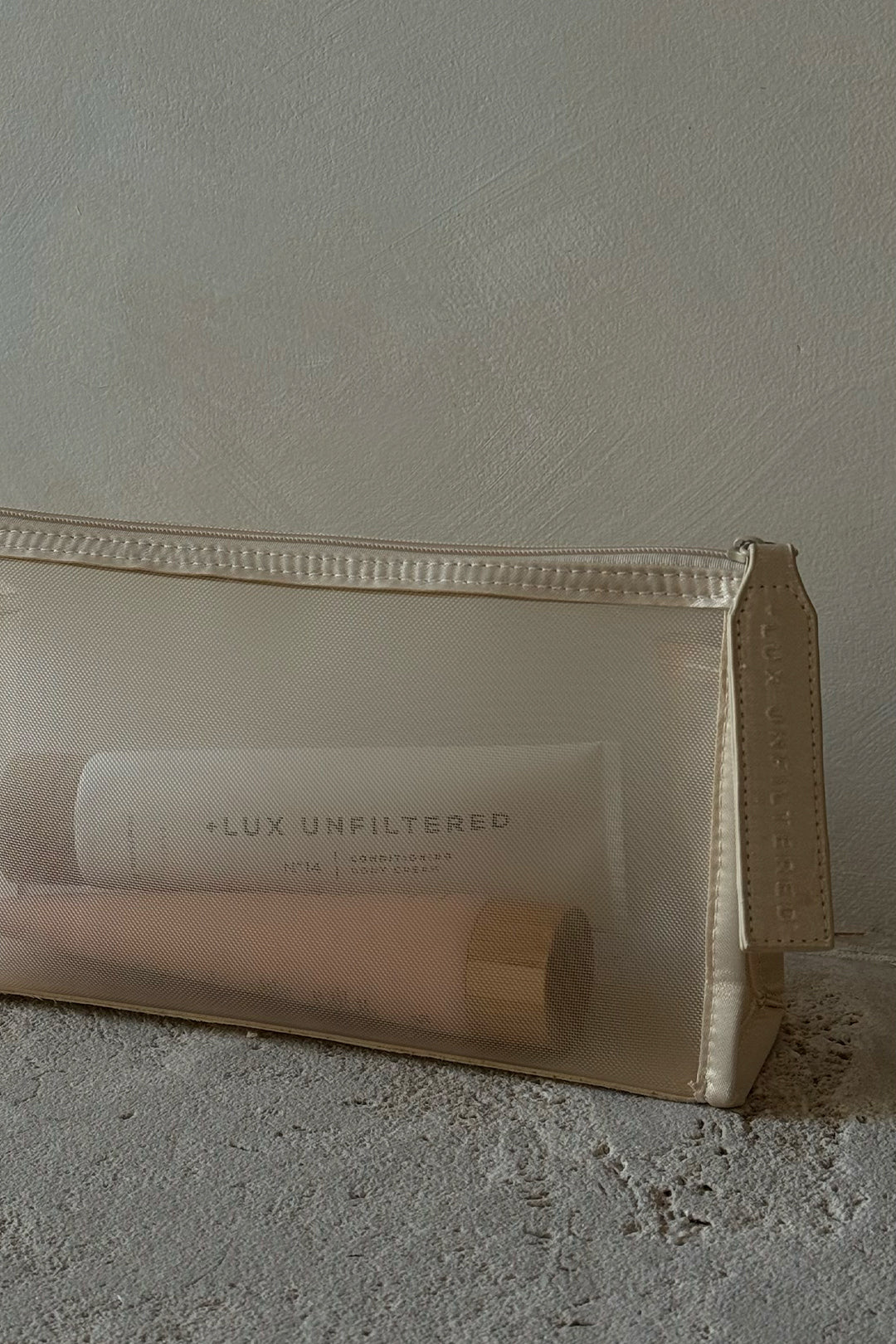 Sheer beige mesh cosmetic pouch with two tubes inside, one labeled LUX UNFILTERED