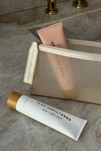 Mesh cosmetic bag holding pink tube and white tube labeled '+ LUX UNFILTERED N°14 CONDITIONING BODY CREAM'; zipper tab reads 'LUX UNFILTERED CO'.