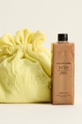 Bottle labeled +LUX UNFILTERED N°30 high gloss SPF 30 OIL BEACH CLUB beside yellow drawstring bag embroidered BOOK the RP