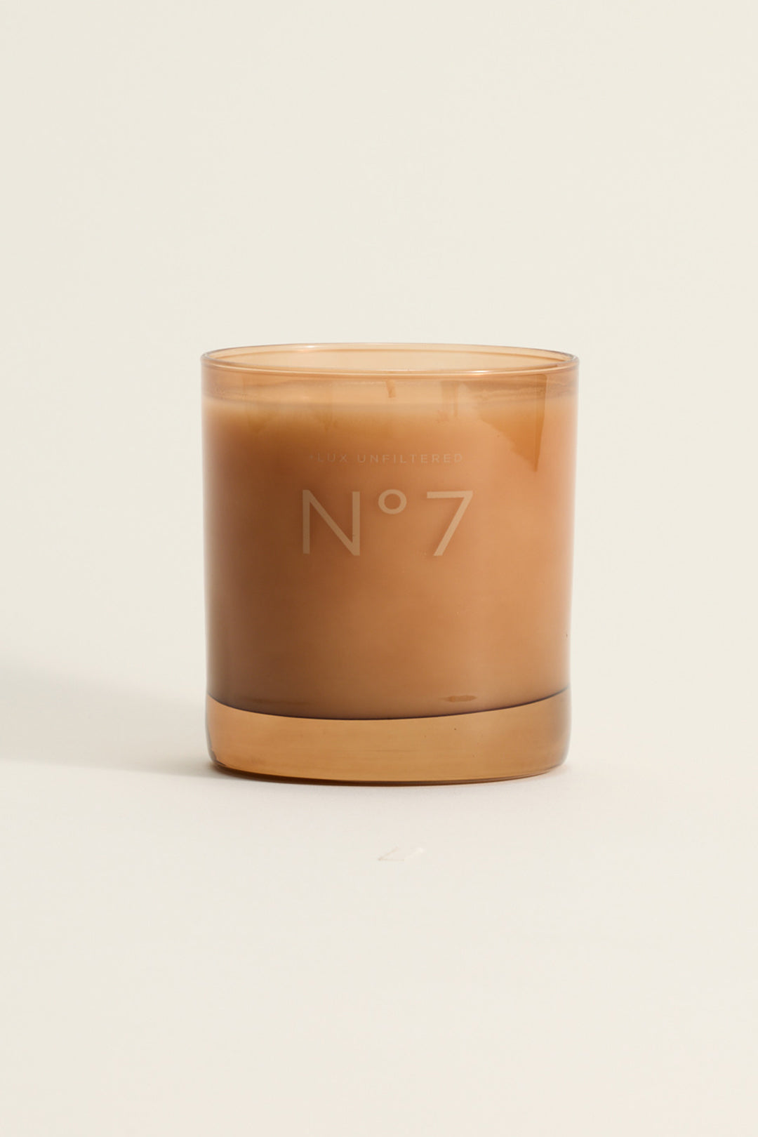 Tan glass candle labeled Nº7 with faint 'LUX UNFILTERED' branding