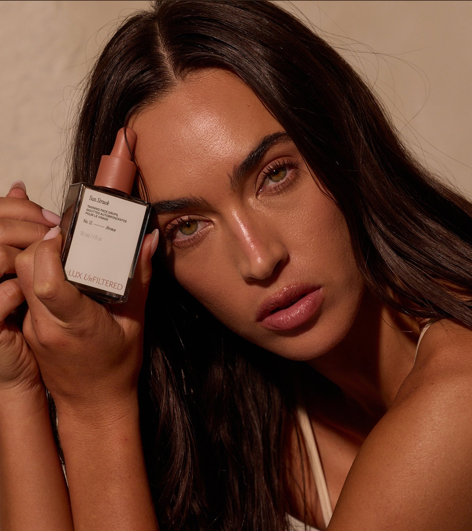 Bronzed woman holding bottle labeled Sun Struck TANNING FACE DROPS No 12 Bronze 30 ml / 1 fl oz LUX UnFILTERED
